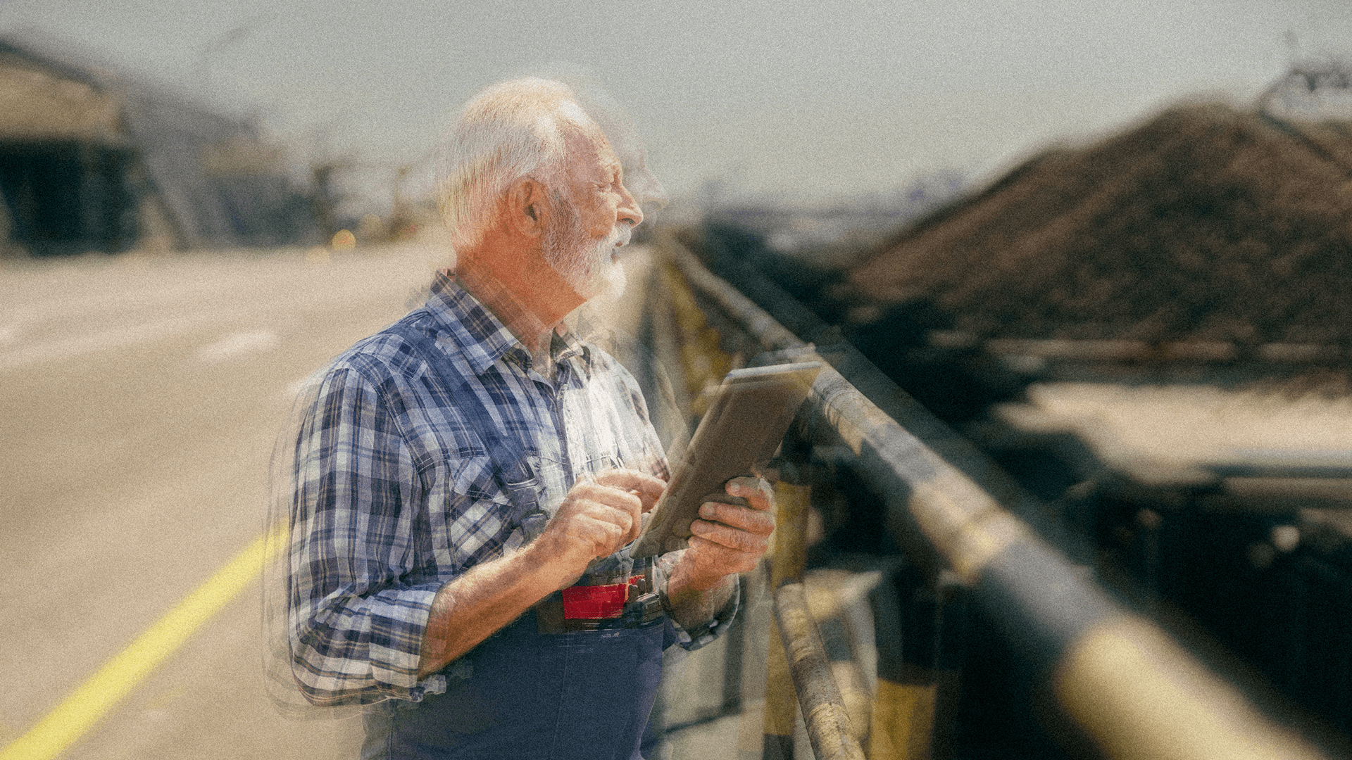 Older engineer using a tablet while inspecting an industrial worksite.