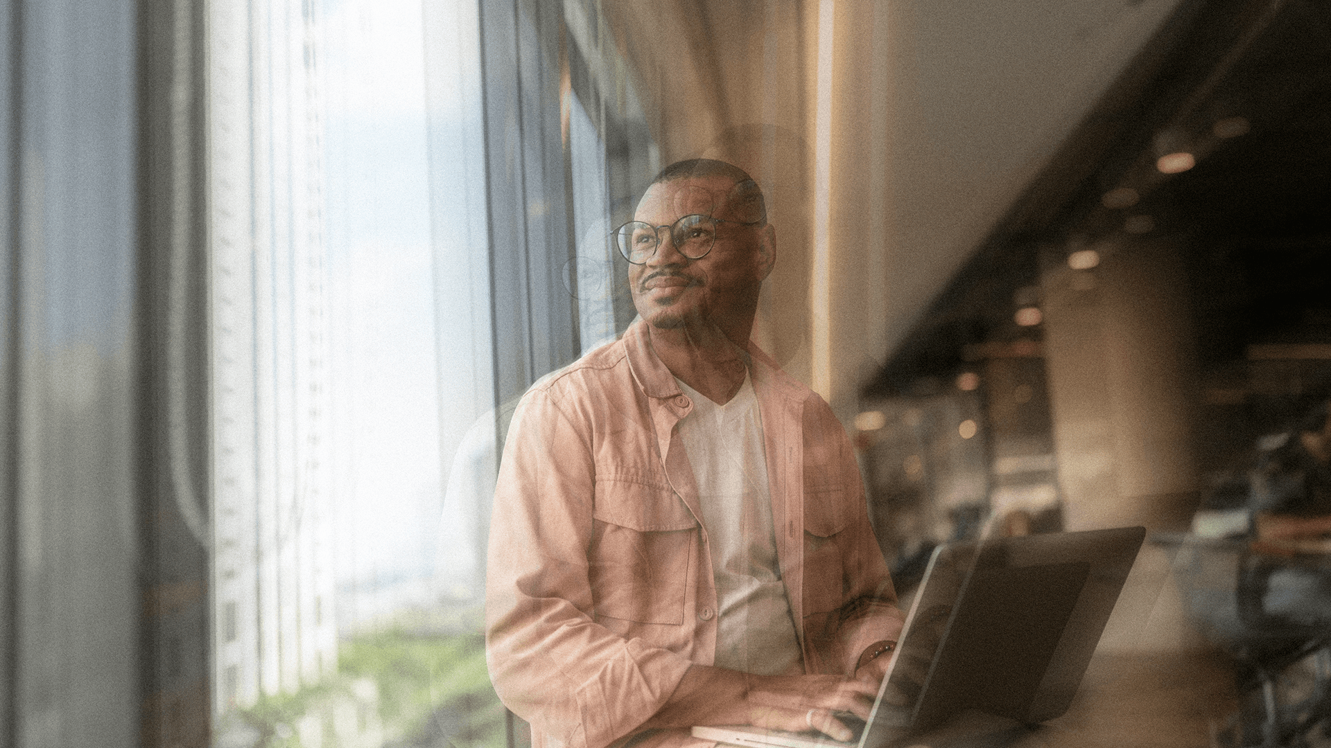 Smiling professional in glasses working on a laptop by a window