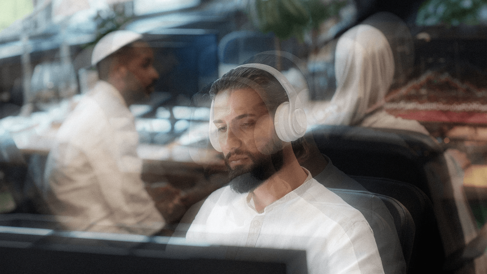Man wearing headphones working on a computer in a busy office environment