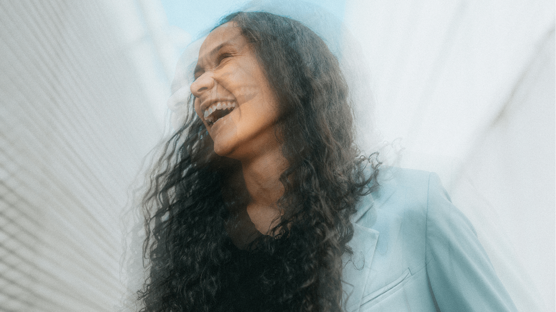 A woman laughing joyfully, captured with soft motion blur against a modern architectural backdrop.