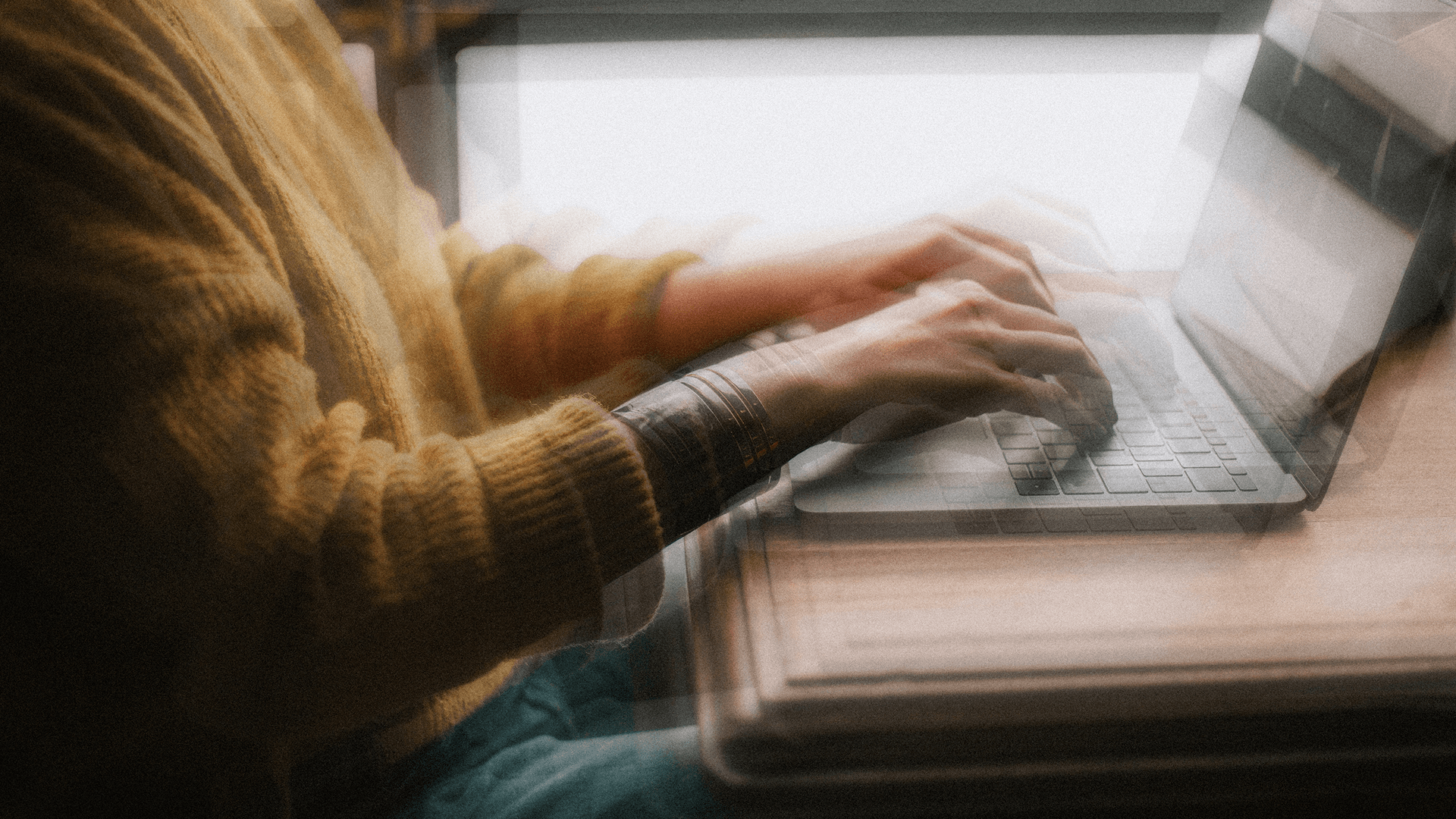 Person in yellow sweater typing on a laptop